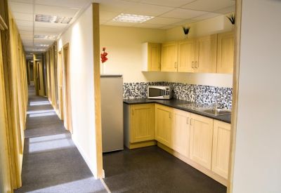 Communal kitchen area with light wood cabinets, patterned backsplash, and a fridge.
