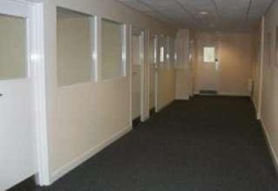 Long carpeted office corridor with white doors and glass partition windows.