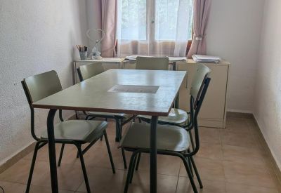 Meeting room with a rectangular table and four green chairs near a window with pink curtains.