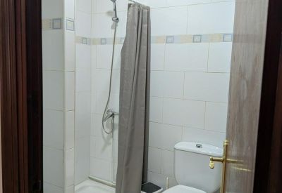 Clean white-tiled bathroom featuring a walk-in shower with a grey curtain.