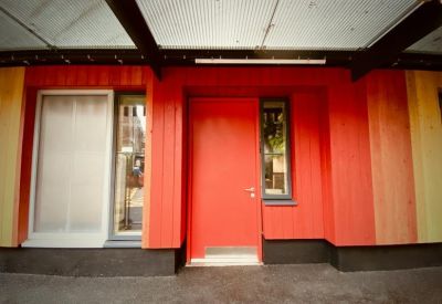 Bright red entrance door set within a multi-colored timber facade.