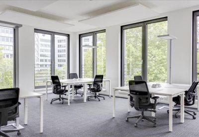 Bright open-plan office with white desks and black mesh chairs near large windows.