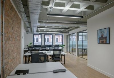 Bright open-plan office space with white desks, black chairs, and an exposed brick feature wall.