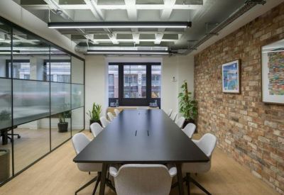 Long boardroom table with grey chairs and a decorative brick wall with framed art.