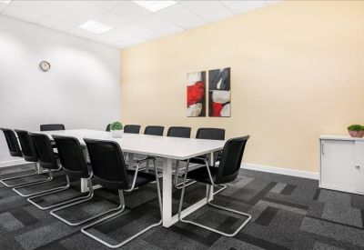 Spacious conference room featuring a long white table, ergonomic black chairs, and neutral toned walls.
