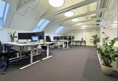 Bright attic workspace with adjustable white desks, dual-monitor setups, and sloped ceilings with windows.