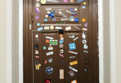 Dark wood interior door decorated with a dense collection of various colorful stickers and logos.