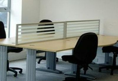 Open-plan office space featuring curved light-wood desks with privacy screens and ergonomic chairs.