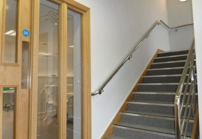 Modern interior corridor with wooden doors, glass partitions, and a staircase with metal handrails.