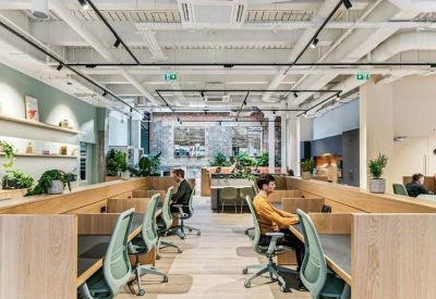 Spacious coworking area with wooden desks, ergonomic green chairs, and indoor plants.