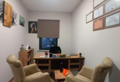 Private office with a wooden desk, armchairs, and certificates on the wall.