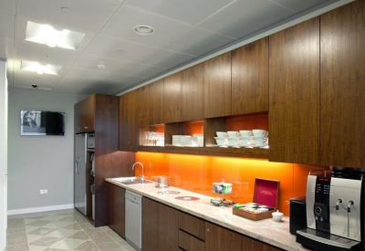 Modern office kitchen with wood cabinetry and an orange glass backsplash.