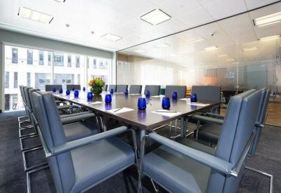 Professional boardroom with a large wooden table, blue chairs, and glass partition walls.
