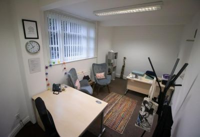 Private office with two desks, grey armchairs, and a striped area rug.