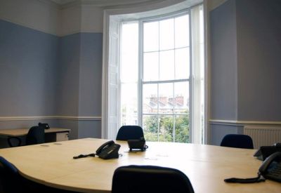 Boardroom with a large light wood table, black chairs, and a period sash window.