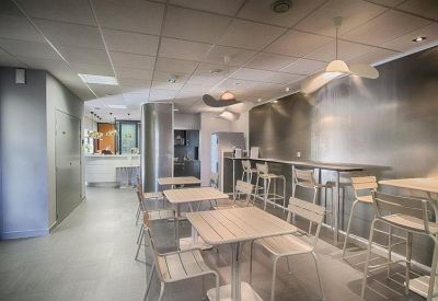 Modern communal dining area with small tables and high stools against a metallic wall.