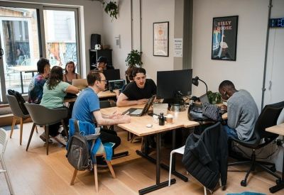 Collaborative office space with people working at shared wooden tables.