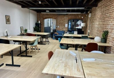 Open-plan coworking space with wooden desks, brick walls, and a blue sofa in the background.