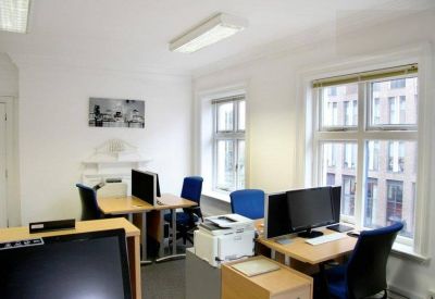 Open-plan workspace with multiple desks, blue chairs, and large windows.