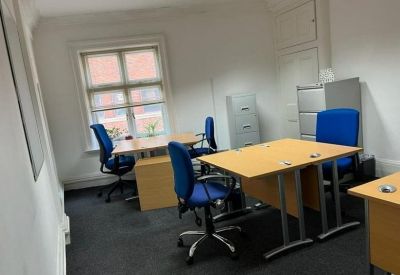 Bright office space featuring wooden desks, blue chairs, and a grey carpet.