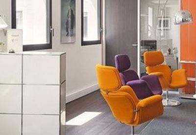 Vibrant reception and waiting area with orange lounge chairs and white modular storage units.