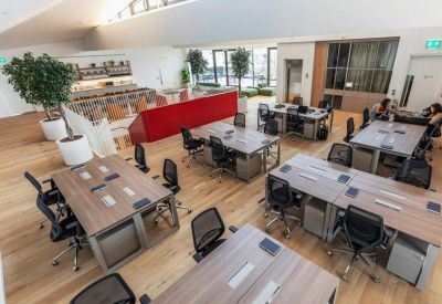 Spacious open-plan office with wooden desks, ergonomic chairs, and large skylights.