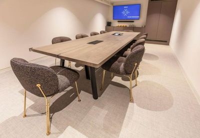 Minimalist meeting room with a large wooden table and grey upholstered chairs.