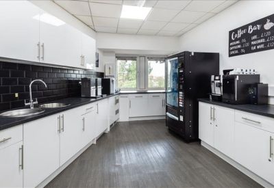 Modern kitchen and communal break area with black tiling and coffee machines.