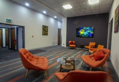 Spacious communal lounge area with orange armchairs, coffee table, and large wall-mounted screen.