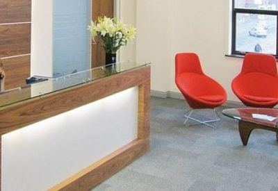 Modern reception desk with wood paneling and bright red designer armchairs.