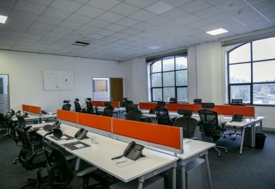 Open-plan office space with rows of white desks and bright orange privacy screens.