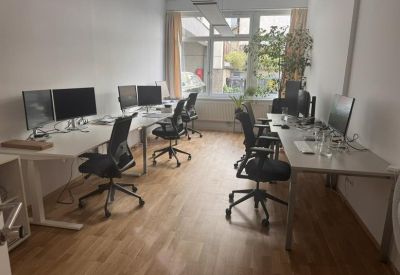 Bright open-plan office with white desks, ergonomic chairs, and wooden flooring.