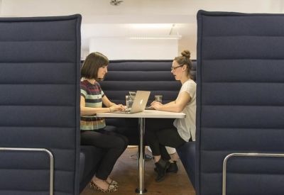 Two people working at a table inside a dark blue high-backed acoustic booth.