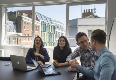 Team meeting around a black table with laptops in front of large windows showing city architecture.