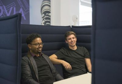 Two colleagues smiling while sitting in a dark blue soundproof semi-private booth.