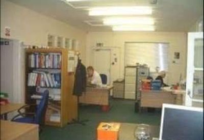 Open-plan office with desks, shelving units, and fluorescent lighting.