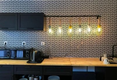 Modern kitchen area featuring patterned wallpaper and a row of industrial pendant lights.