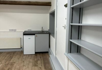 Functional kitchenette area with a sink and mini-fridge situated under a sloping ceiling with built-in shelving.