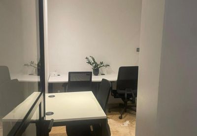 Private glass-walled office with white desks and black ergonomic chairs.