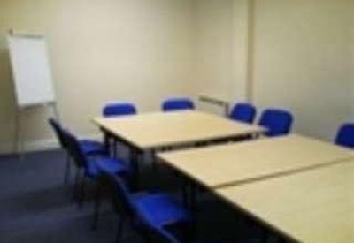 Meeting room with blue chairs around two light wood tables and a flipchart.