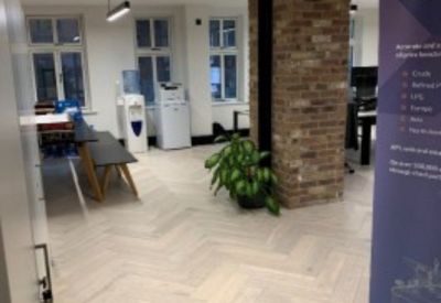 Bright communal break area with herringbone wood floors, a water station, and brick pillars.