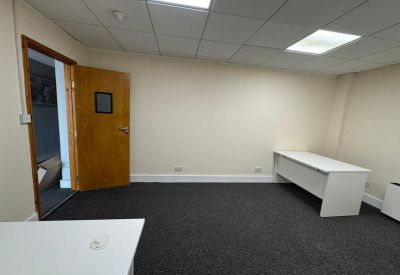 Bright internal office room with white walls and a wooden door leading to a hallway.