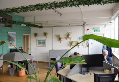 Open-plan coworking space with large windows, wall-mounted plants, and multiple workstations.