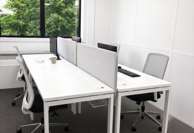 Open-plan office with white workstations, fabric dividers, and views of lush green trees.