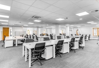 Bright open-plan office with rows of white desks and black ergonomic chairs.
