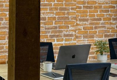 Office workstations featuring wooden desks and ergonomic chairs against a brick wall.