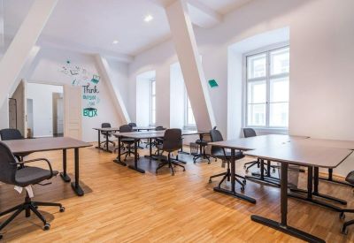 Spacious open-plan office with multiple workstations, light wood floors, and vaulted ceiling beams.