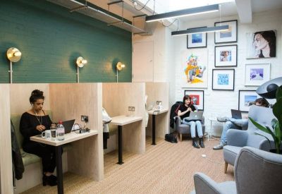 Individual workstations with wooden partitions and comfortable armchairs against a gallery wall.