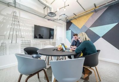 Bright breakout space with people working at a round table near a colorful wall mural.
