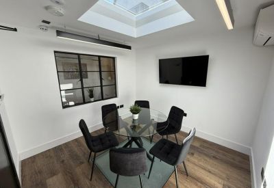Meeting room with a round glass table, black chairs, and a large wall-mounted screen.